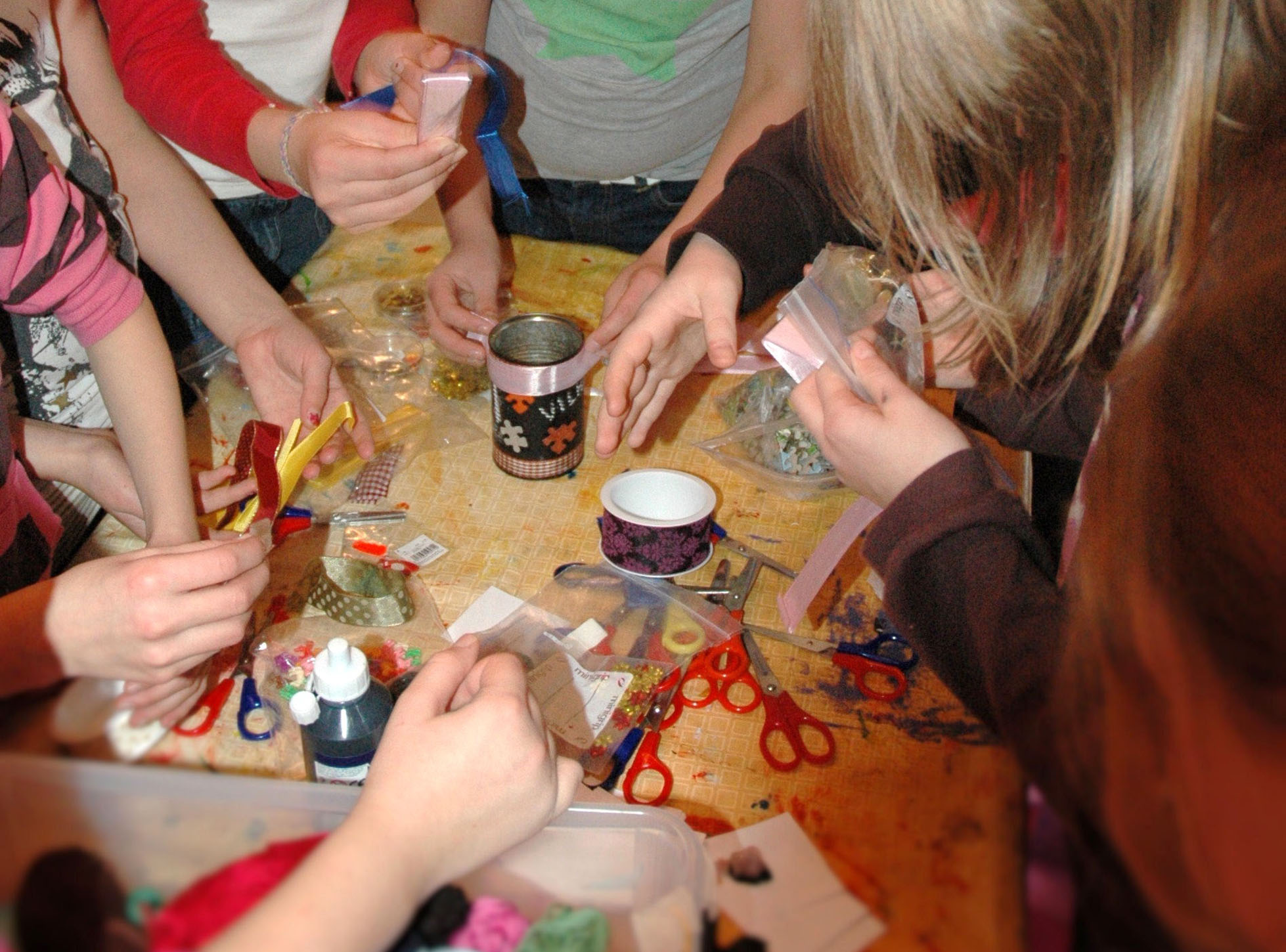 Lasten kädet tavoittelevat askartelutarvikkeita pöydällä