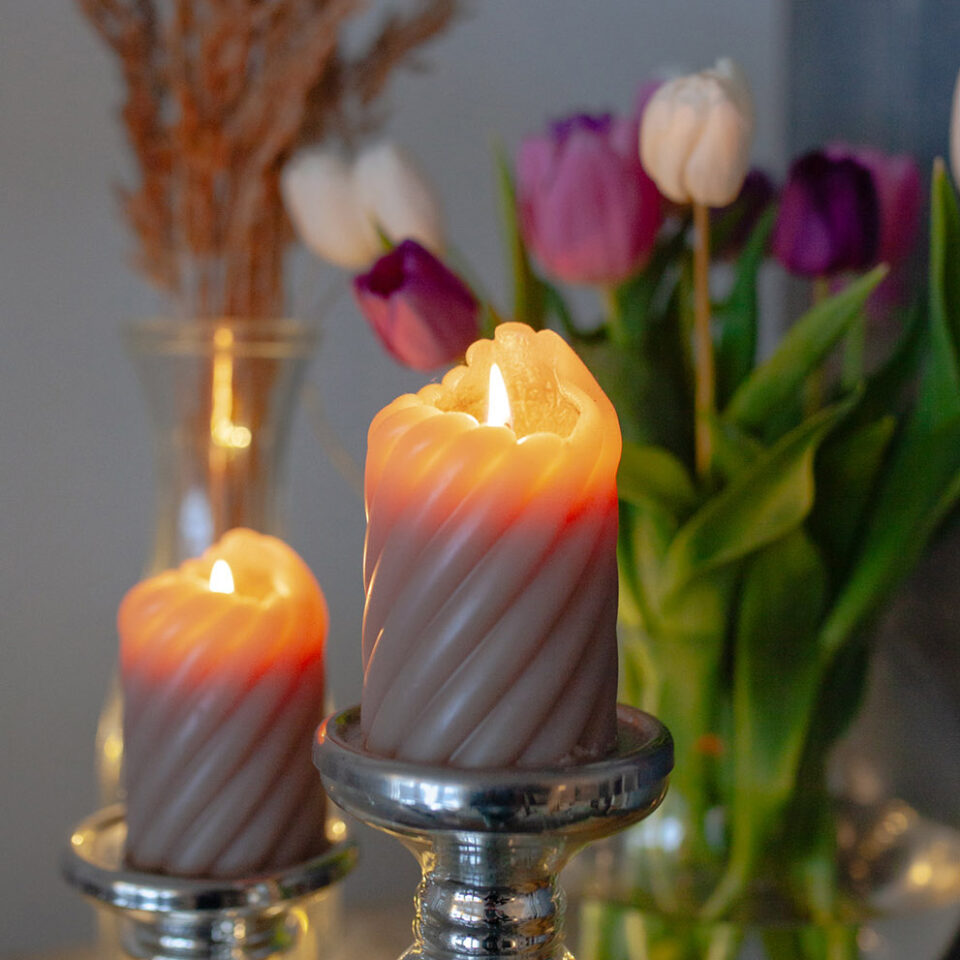 Kaksi kynttilää palaa, taustalla tulppaaneja maljakossa.