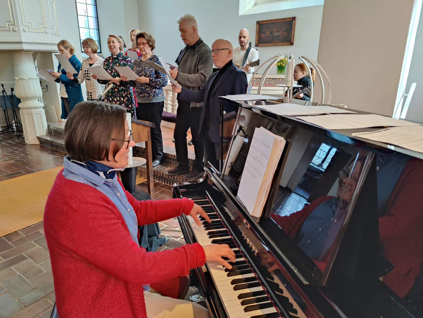 Kanttori Niina Venäläinen soittaa pianoa ja seurakunnan työntekijöitä laulamassa Marian kirkossa alttarin edessä.