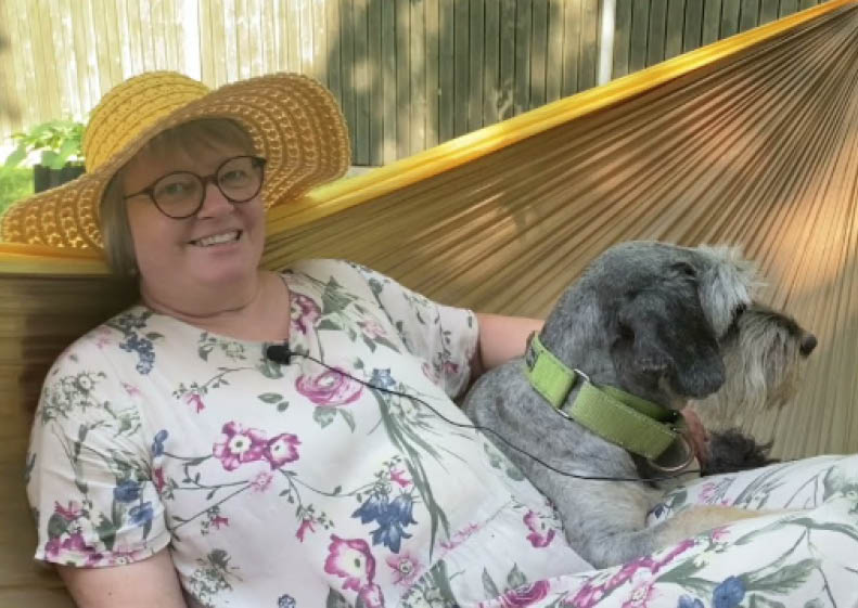 Kirsti Malmi istuu koiran kanssa pihakeinussa.
