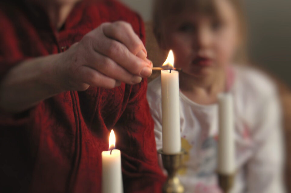 Nainen sytyttää kaksi adventtikynttilää. Lapsi seuraa vierestä.
