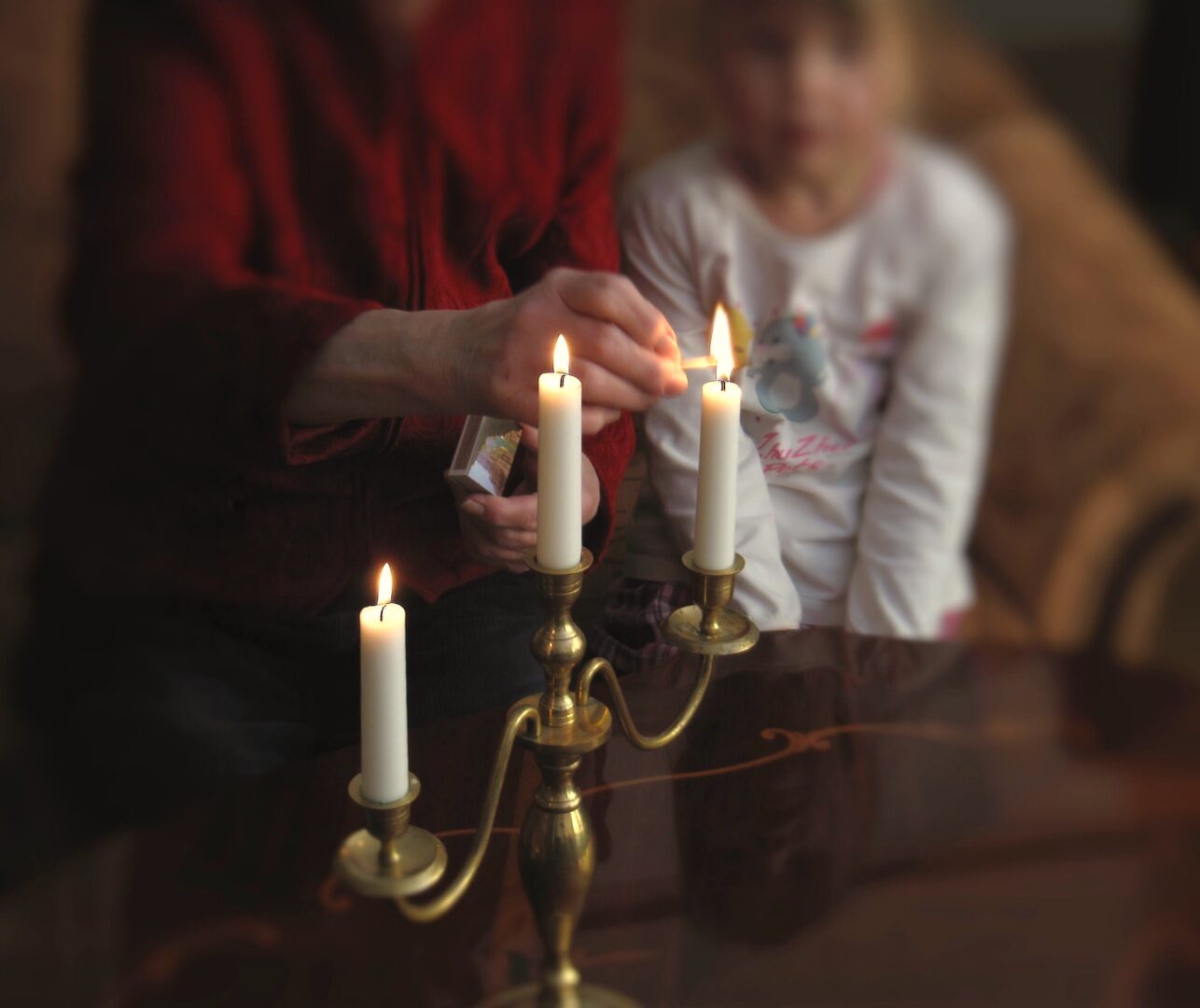 Nainen sytyttää kolmannen adventtikynttilän. Pieni tyttö seuraa vierestä.