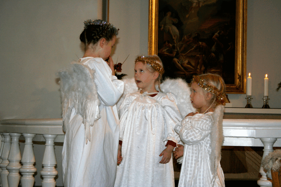 Kolme lasta pukeutuneet enkeleiksi. Seisovat Marian kirkon alttarin edessä.