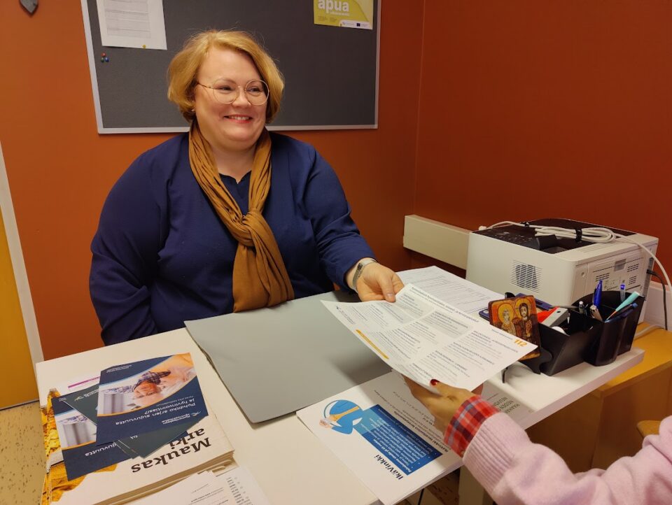 Diakoniaviranhaltija Eva Andersen ojentaa lomaketta työpöydän yli asiakkaalleen.